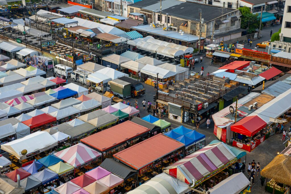 Colorful aerial view of bustling market stalls with diverse canopies and people shopping.